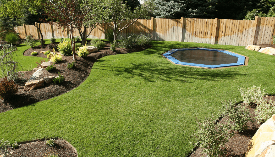 Manicured back yard with landscaped beds of mulch and plants and an in-ground trampoline.